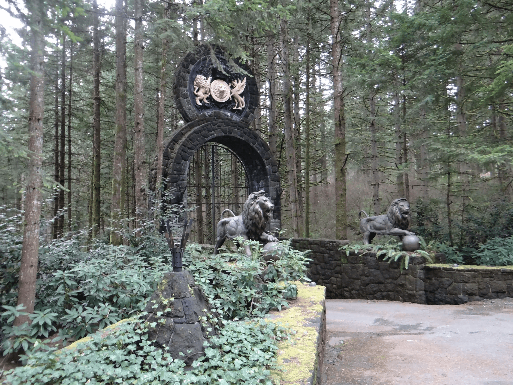 The stone gate arch with its crest and two bronze lion statues seen from the side among mossy walls